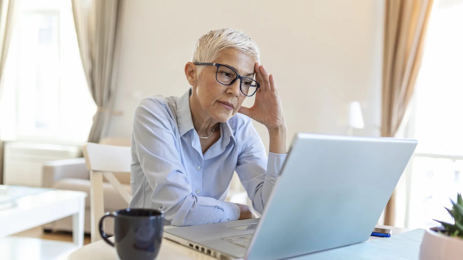 Older woman with glasses looking at her laptop with a concerned expression